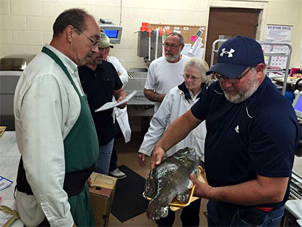 Bruce Kraemer (Center rear) looks on as his giant smallmouth bass is prepared for the official weigh in.