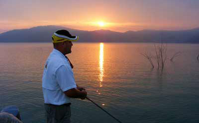Sun sets on an angler fishing thorn trees on giant bass Mexican bass lake Comedero.